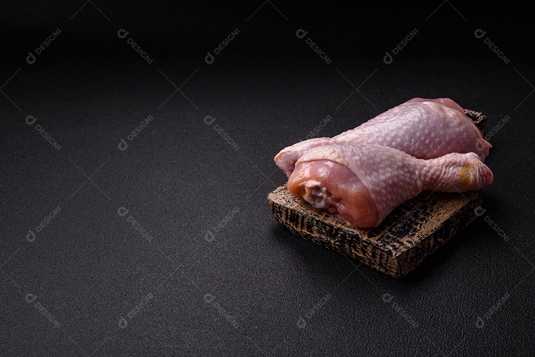 Pernas de frango cru com sal, especiarias e ervas sobre um fundo escuro de concreto