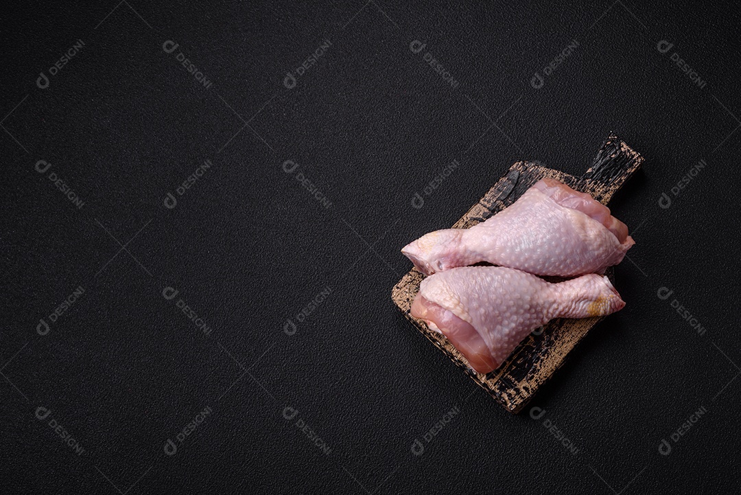 Pernas de frango cru com sal, especiarias e ervas sobre um fundo escuro de concreto