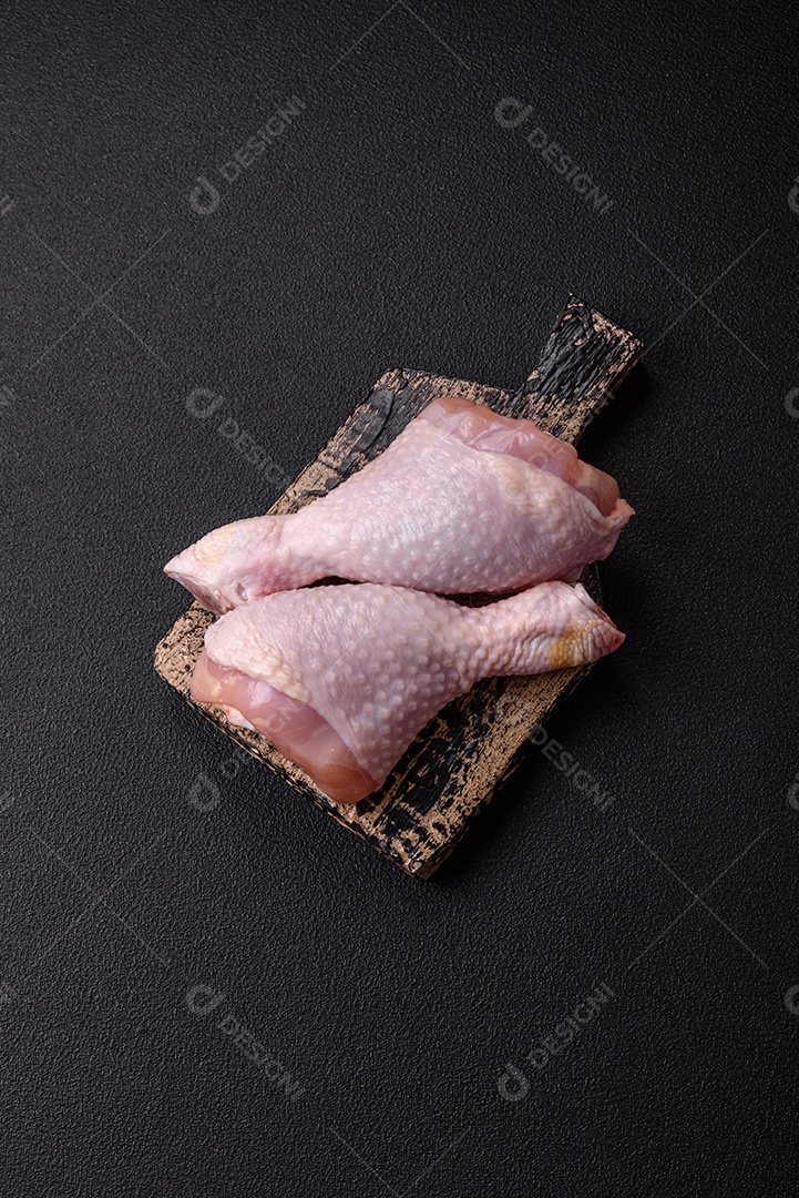 Pernas de frango cru com sal, especiarias e ervas sobre um fundo escuro de concreto