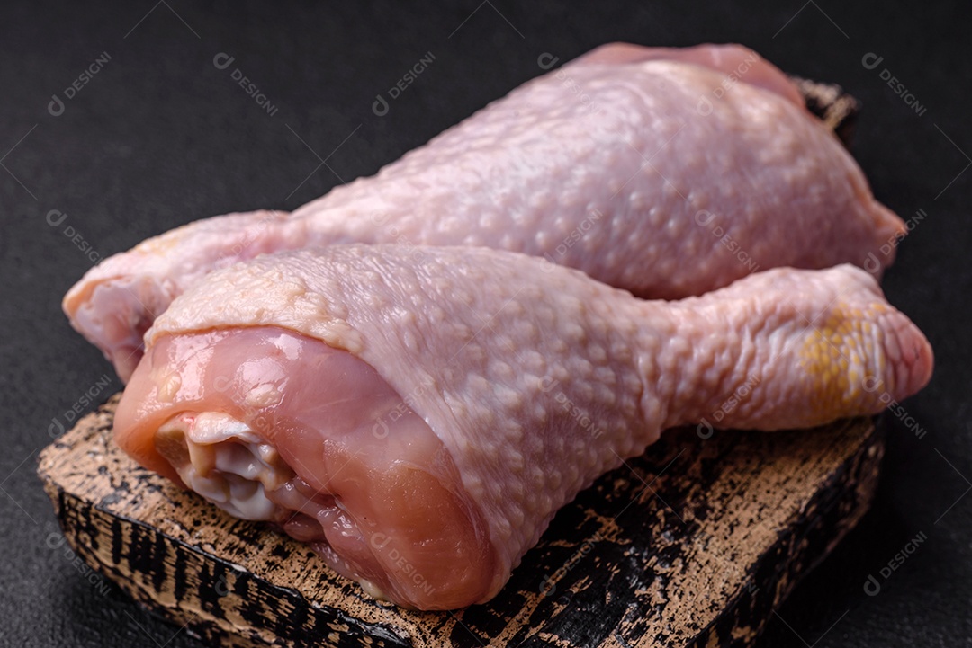 Pernas de frango cru com sal, especiarias e ervas sobre um fundo escuro de concreto