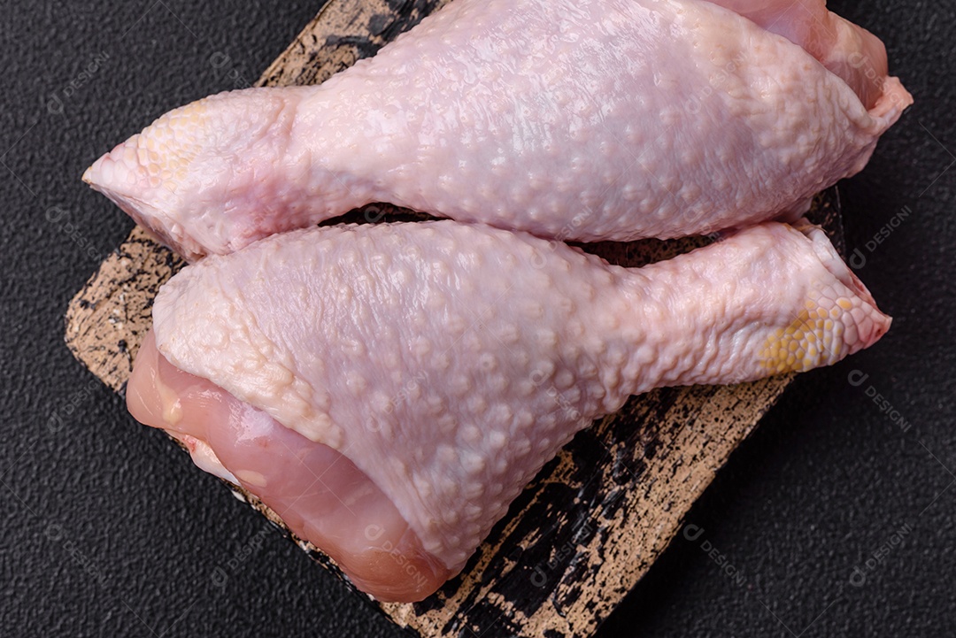 Pernas de frango cru com sal, especiarias e ervas sobre um fundo escuro de concreto