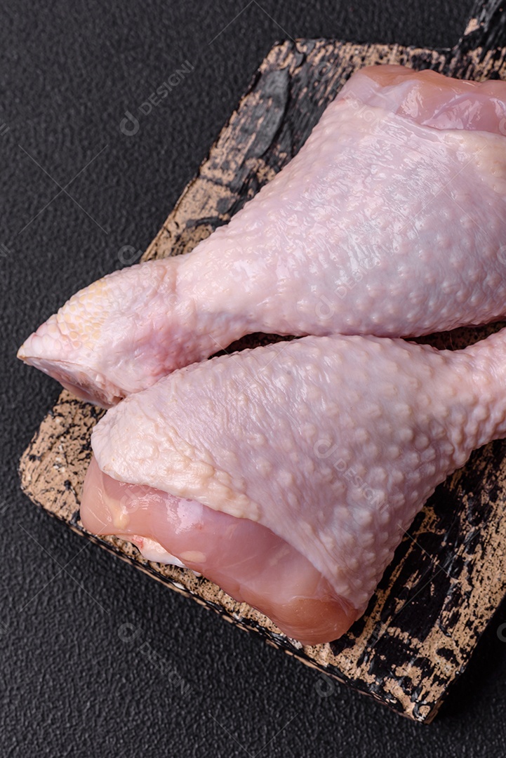 Pernas de frango cru com sal, especiarias e ervas sobre um fundo escuro de concreto