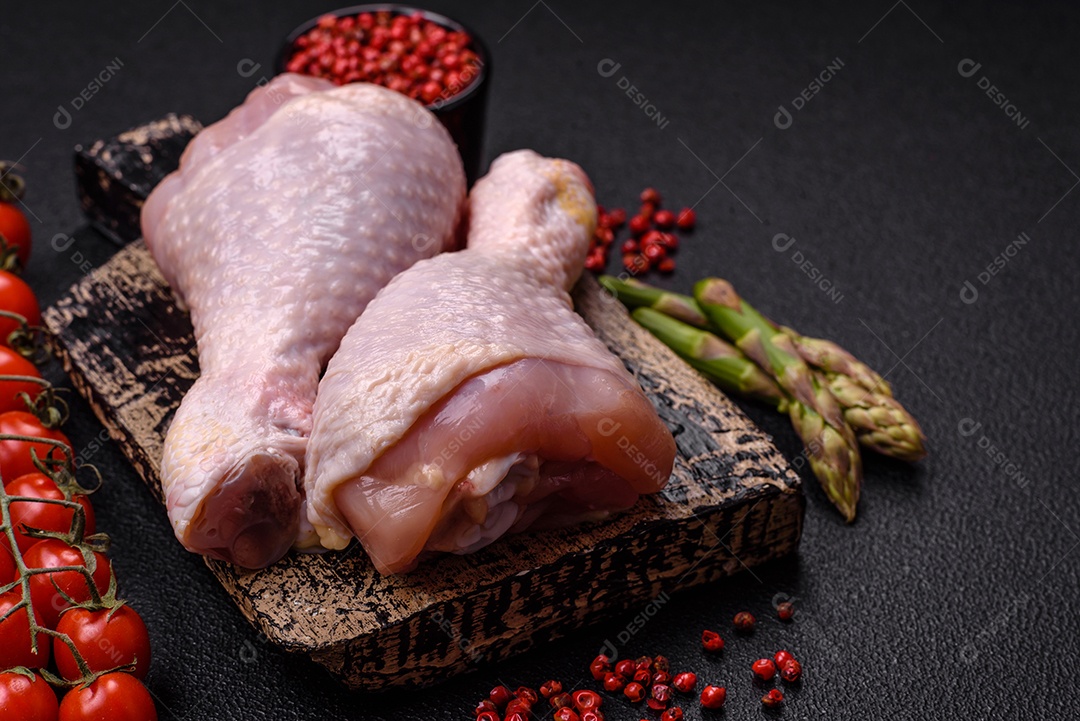 Pernas de frango cru com sal, especiarias e ervas sobre um fundo escuro de concret