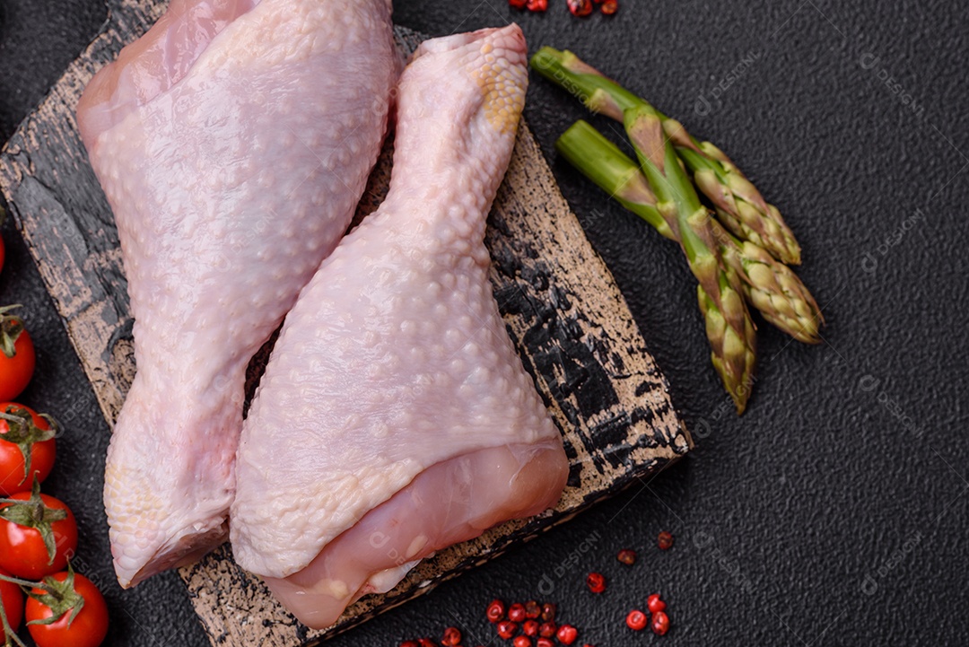 Pernas de frango cru com sal, especiarias e ervas sobre um fundo escuro de concreto