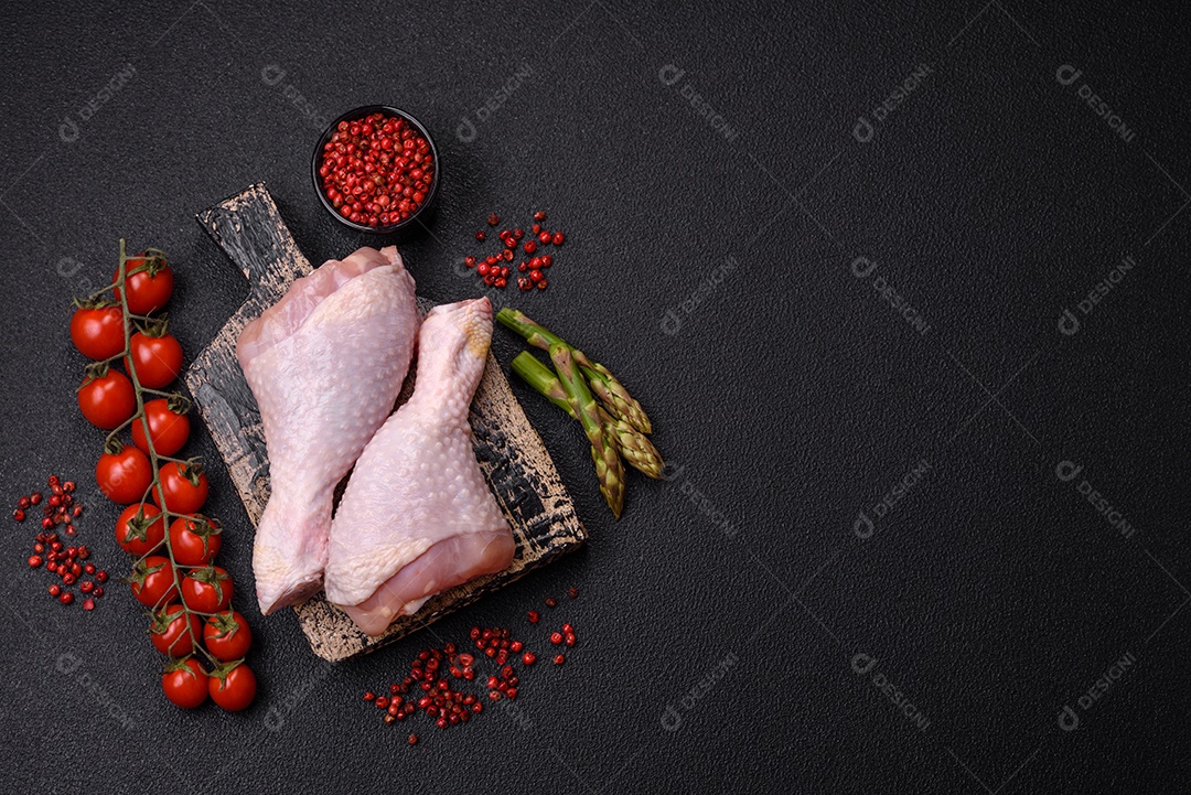 Pernas de frango cru com sal, especiarias e ervas sobre um fundo escuro de concreto