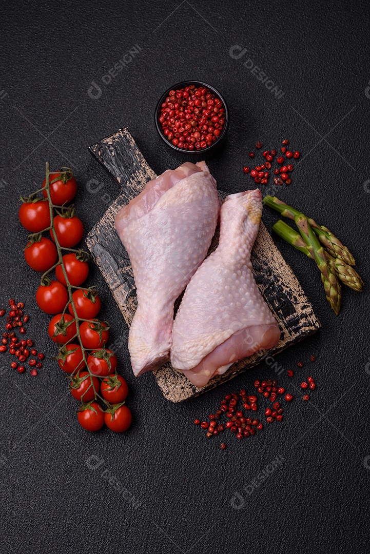 Pernas de frango cru com sal, especiarias e ervas sobre um fundo escuro de concreto