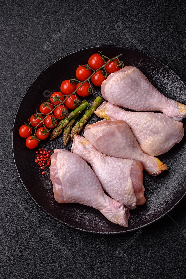 Pernas de frango cru com sal, especiarias e ervas sobre um fundo escuro de concreto