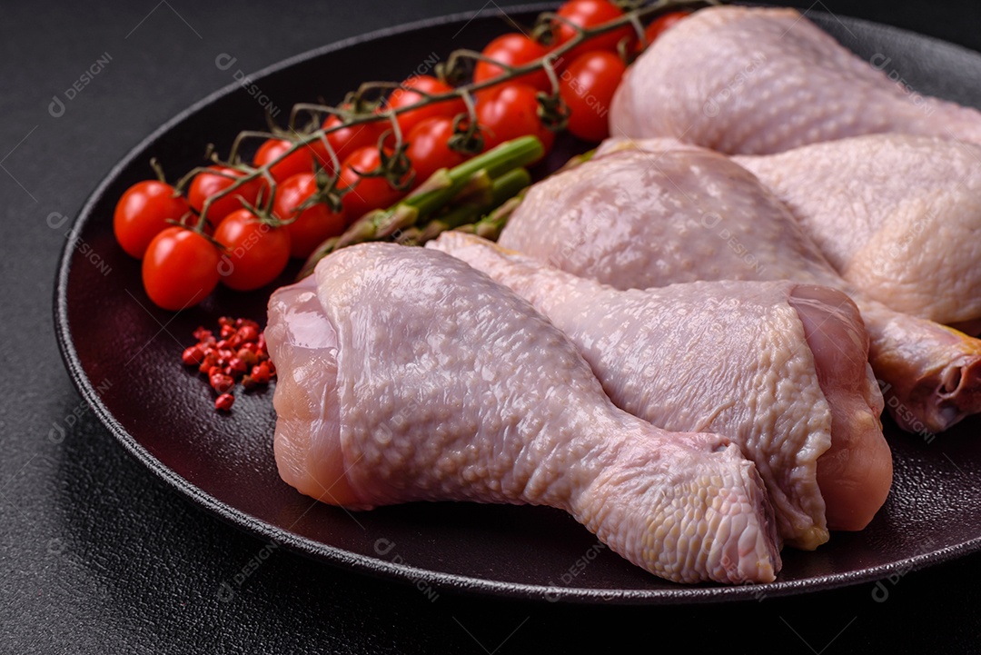 Pernas de frango cru com sal, especiarias e ervas sobre um fundo escuro de concreto