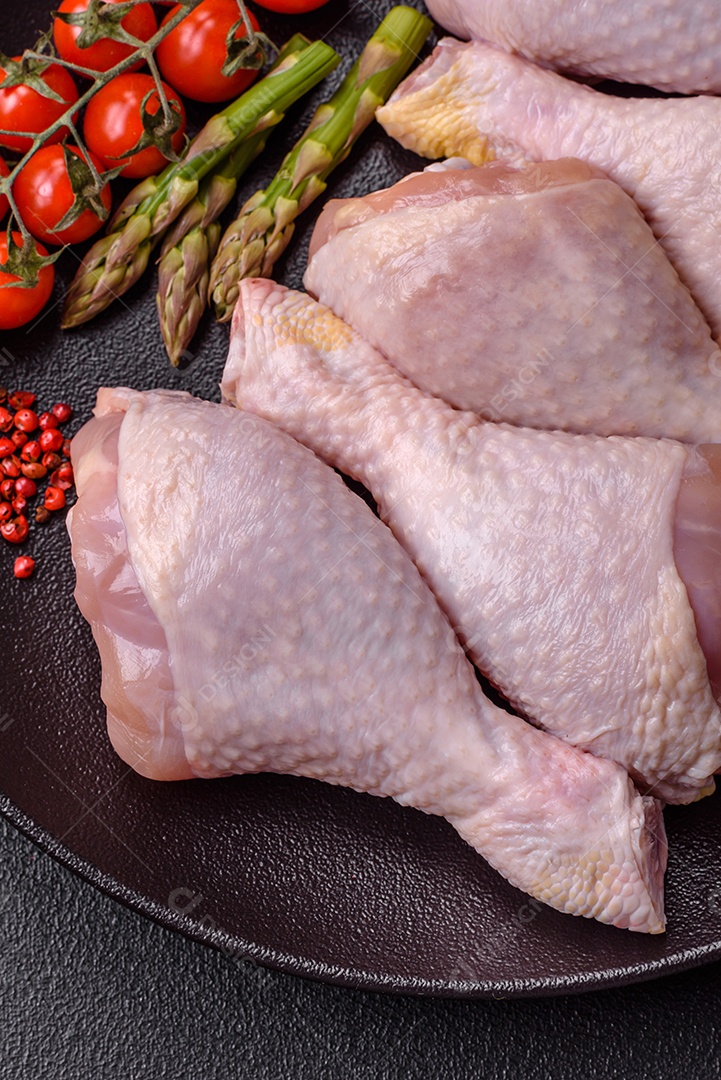 Pernas de frango cru com sal, especiarias e ervas sobre um fundo escuro de concreto