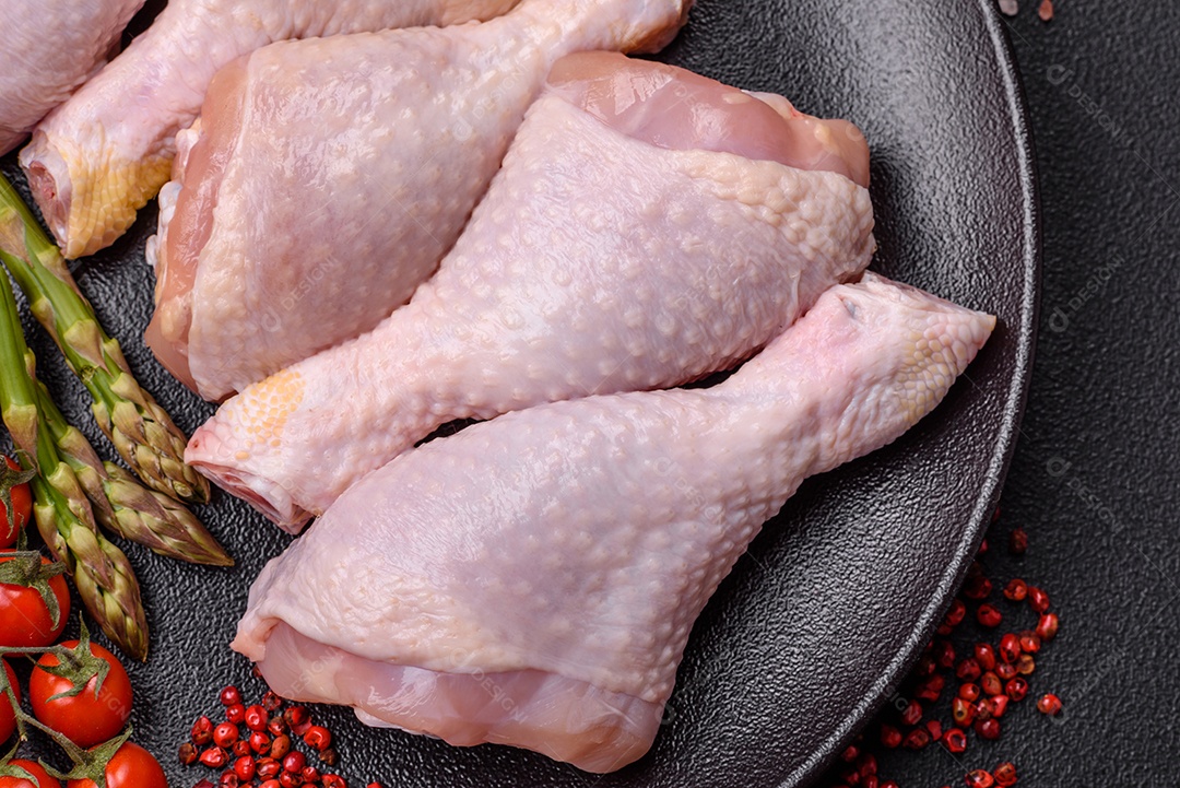 Pernas de frango cru com sal, especiarias e ervas sobre um fundo escuro de concreto