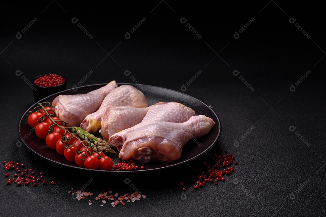 Pernas de frango cru com sal, especiarias e ervas sobre um fundo escuro de concreto