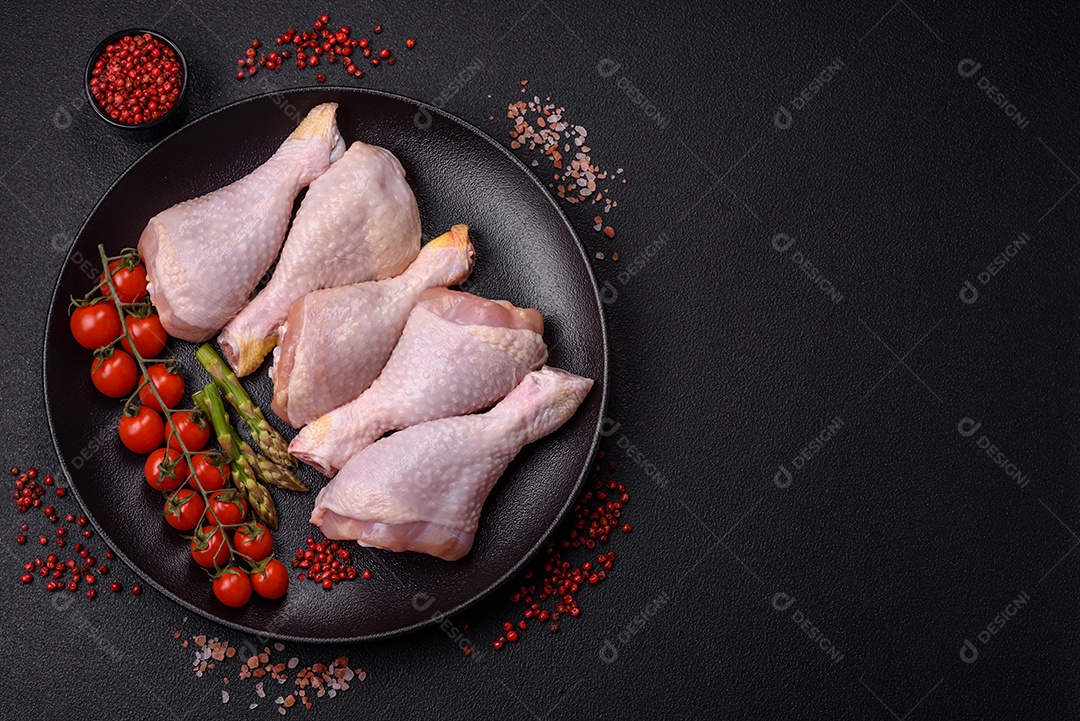 Pernas de frango cru com sal, especiarias e ervas sobre um fundo escuro de concreto
