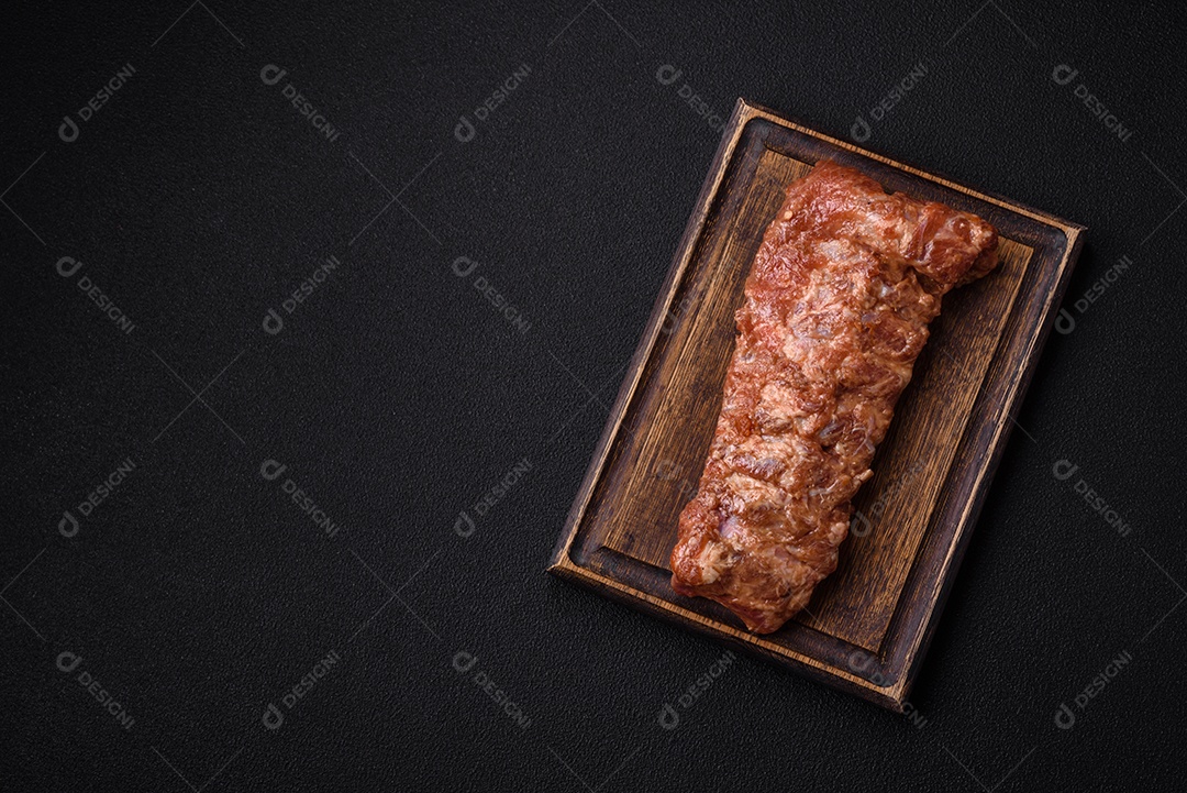 Costelas de porco cruas marinadas com sal, especiarias e ervas sobre um fundo escuro de concreto