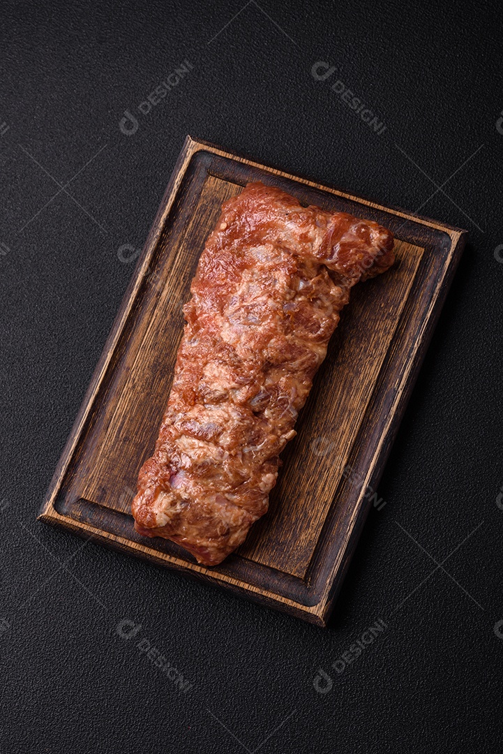 Costelas de porco cruas marinadas com sal, especiarias e ervas sobre um fundo escuro de concreto