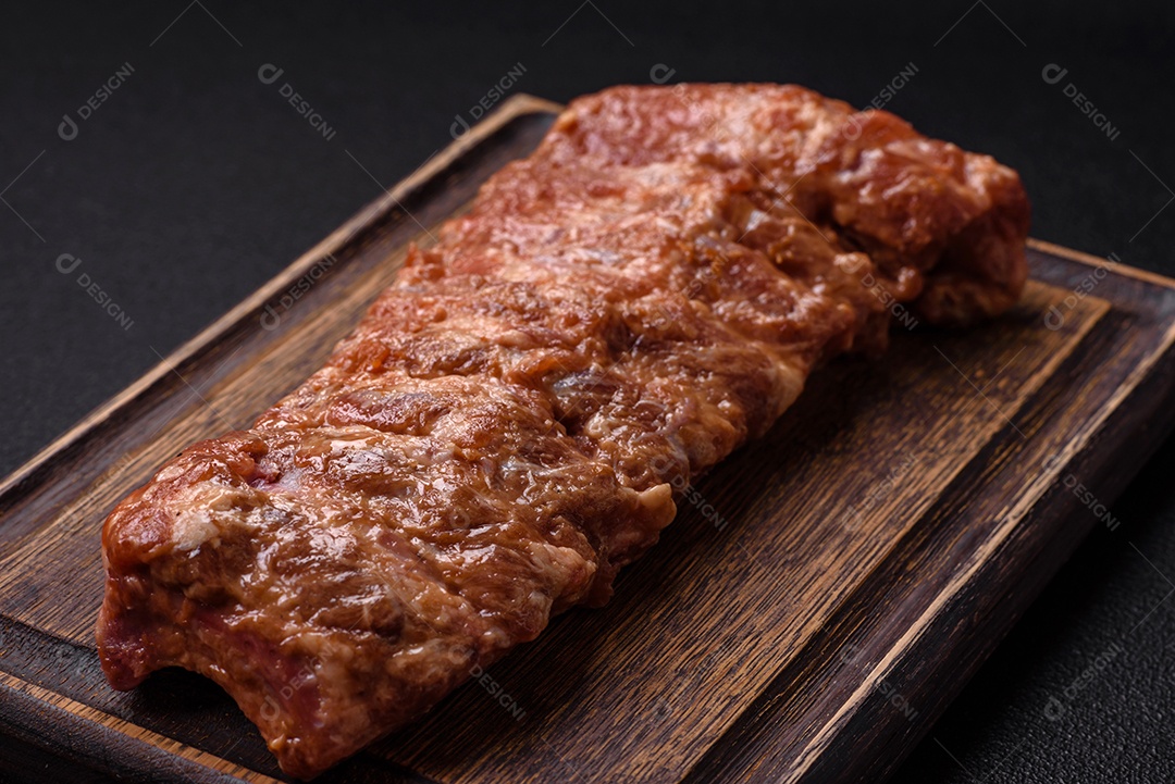 Costelas de porco cruas marinadas com sal, especiarias e ervas sobre um fundo escuro de concreto