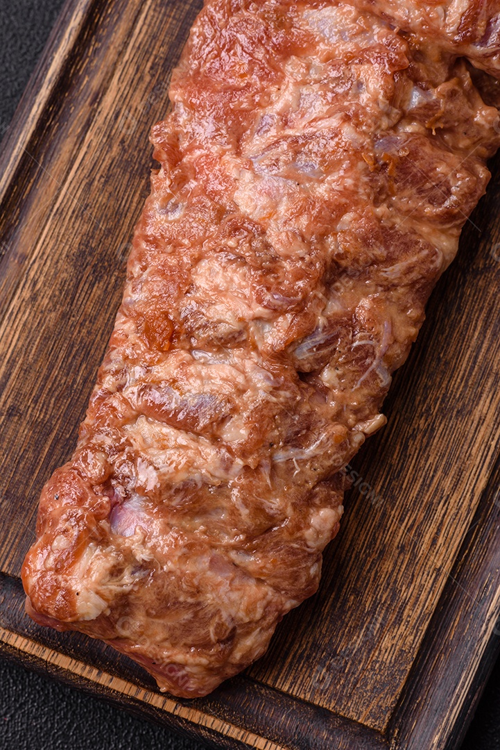 Costelas de porco cruas marinadas com sal, especiarias e ervas sobre um fundo escuro de concreto