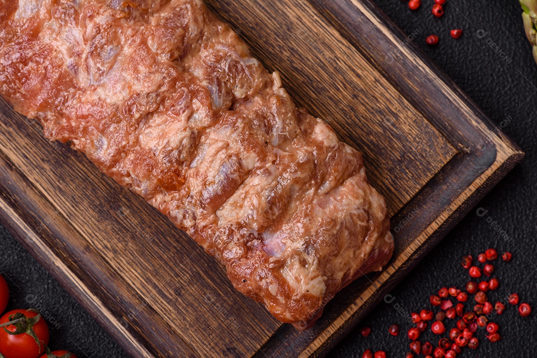 Costelas de porco cruas marinadas com sal, especiarias e ervas sobre um fundo escuro de concreto