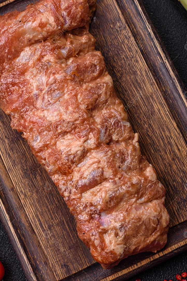 Costelas de porco cruas marinadas com sal, especiarias e ervas sobre um fundo escuro de concreto