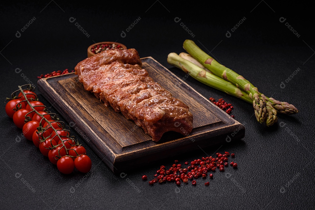 Costelas de porco cruas marinadas com sal, especiarias e ervas sobre um fundo escuro de concreto