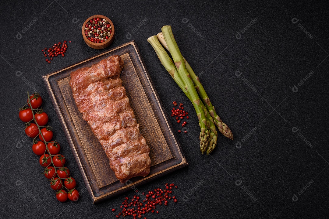 Costelas de porco cruas marinadas com sal, especiarias e ervas sobre um fundo escuro de concreto