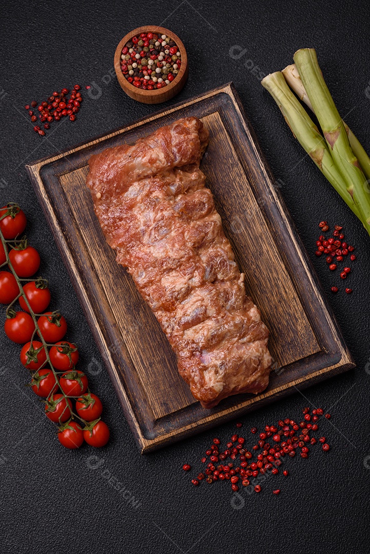 Costelas de porco cruas marinadas com sal, especiarias e ervas sobre um fundo escuro de concreto