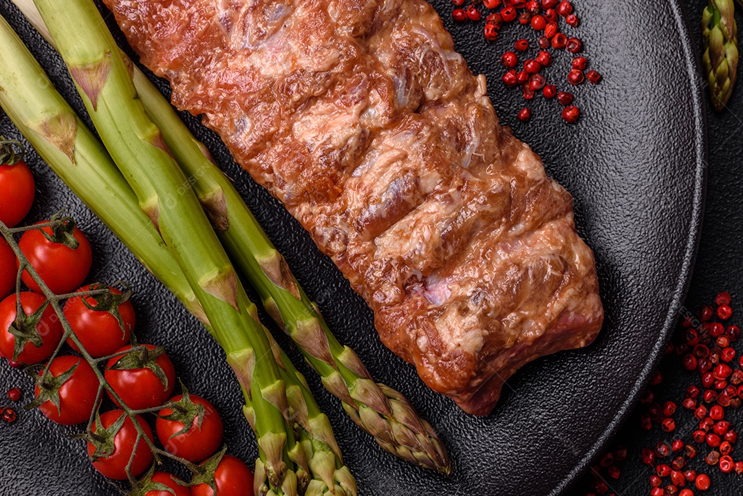 Costelas de porco cruas marinadas com sal, especiarias e ervas sobre um fundo escuro de concreto