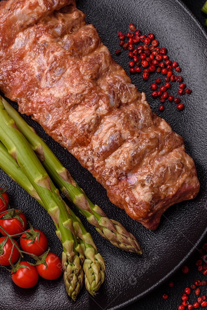 Costelas de porco cruas marinadas com sal, especiarias e ervas sobre um fundo escuro de concreto