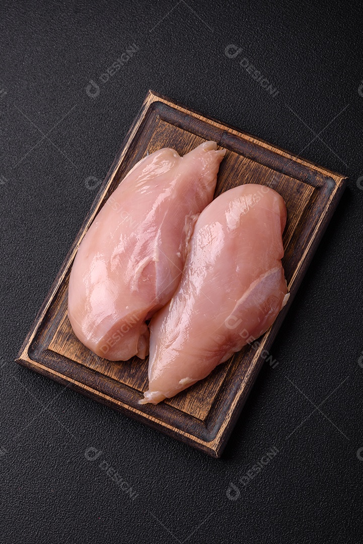 Filé de frango cru com sal, especiarias e ervas sobre um fundo escuro de concreto