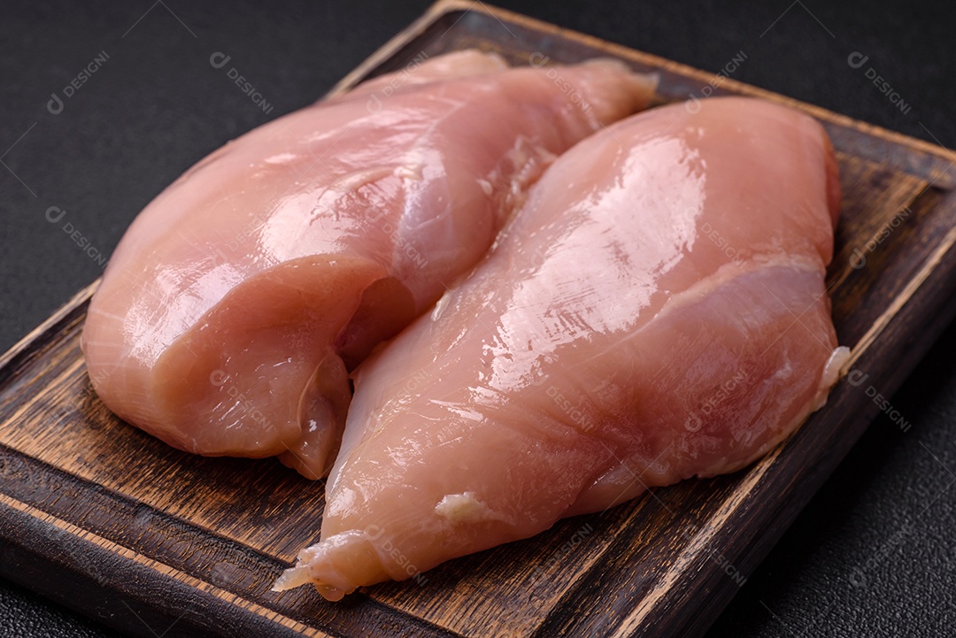 Filé de frango cru com sal, especiarias e ervas sobre um fundo escuro de concreto