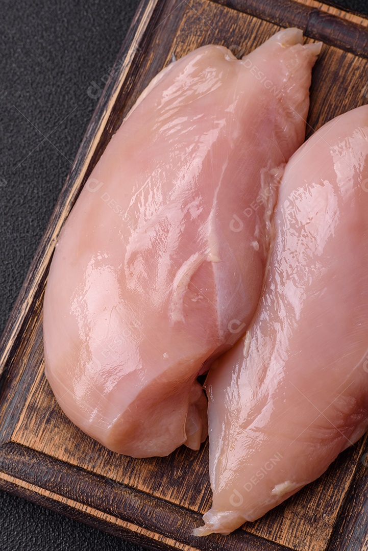 Filé de frango cru com sal, especiarias e ervas sobre um fundo escuro de concreto