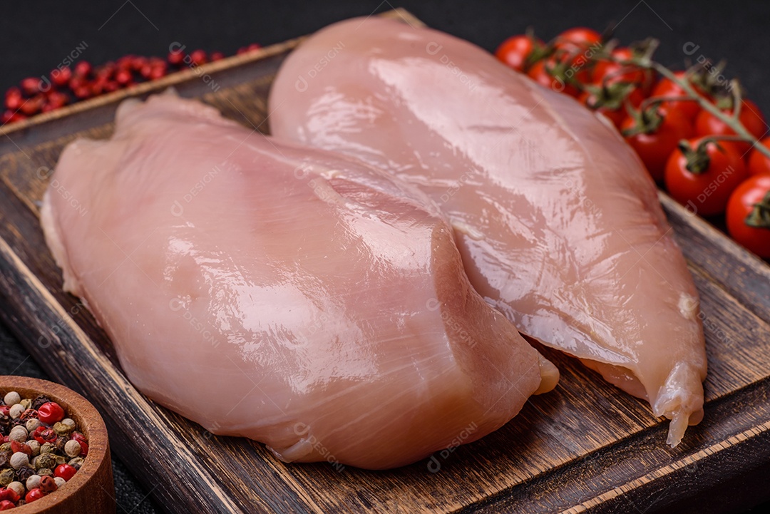 Filé de frango cru com sal, especiarias e ervas sobre um fundo escuro de concreto