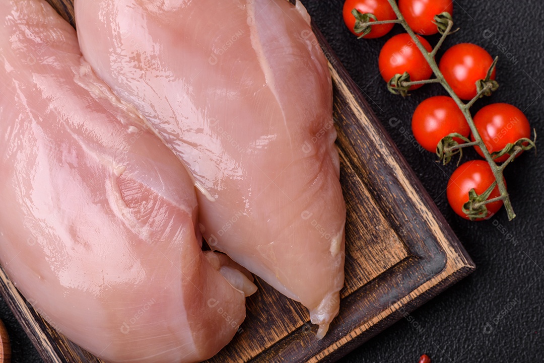 Filé de frango cru com sal, especiarias e ervas sobre um fundo escuro de concreto