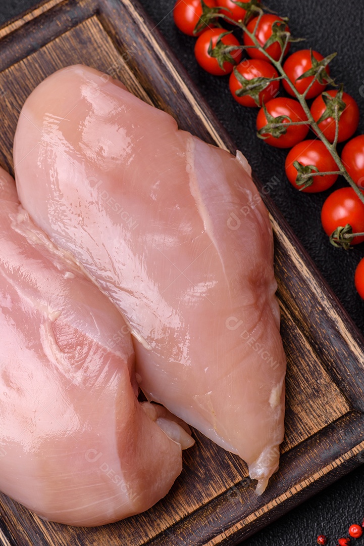 Filé de frango cru com sal, especiarias e ervas sobre um fundo escuro de concreto