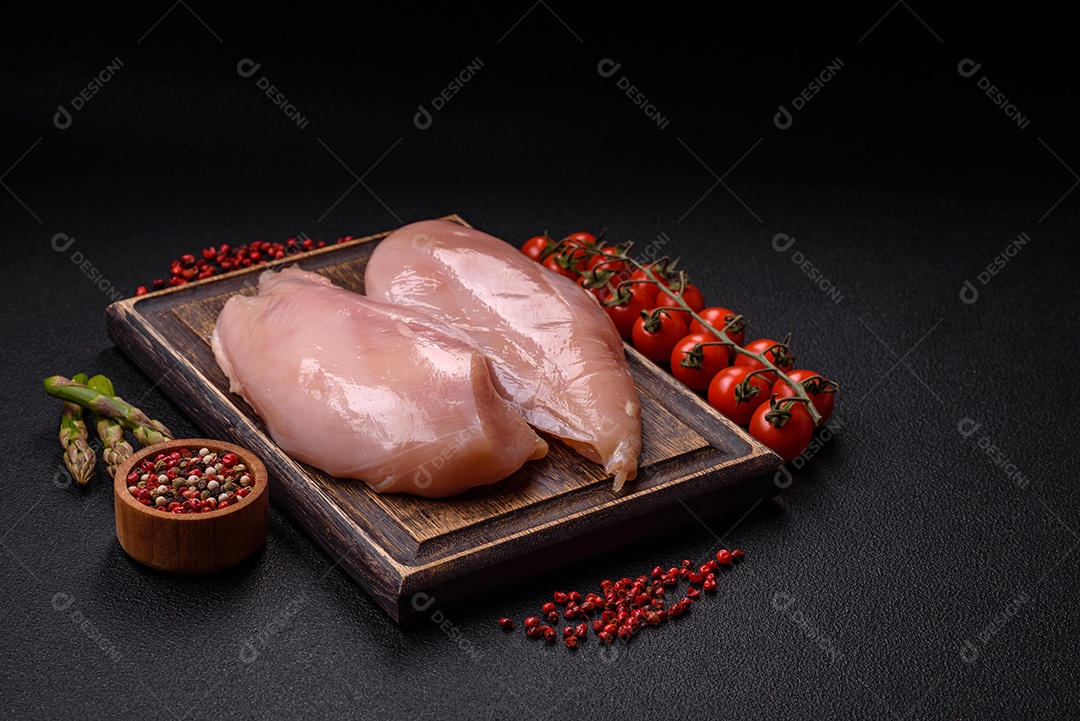 Filé de frango cru com sal, especiarias e ervas sobre um fundo escuro de concreto