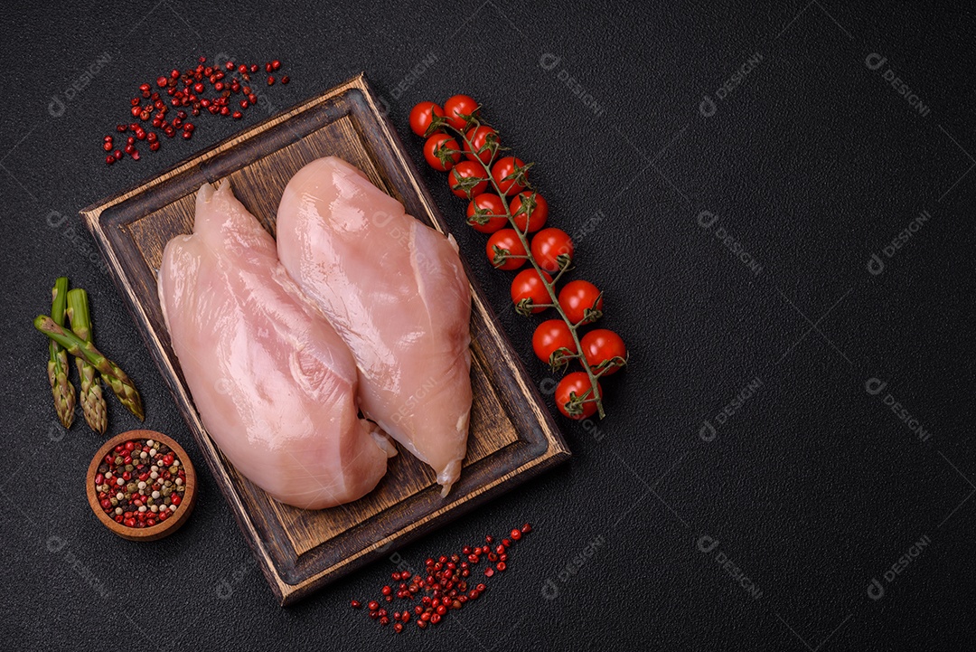 Filé de frango cru com sal, especiarias e ervas sobre um fundo escuro de concreto