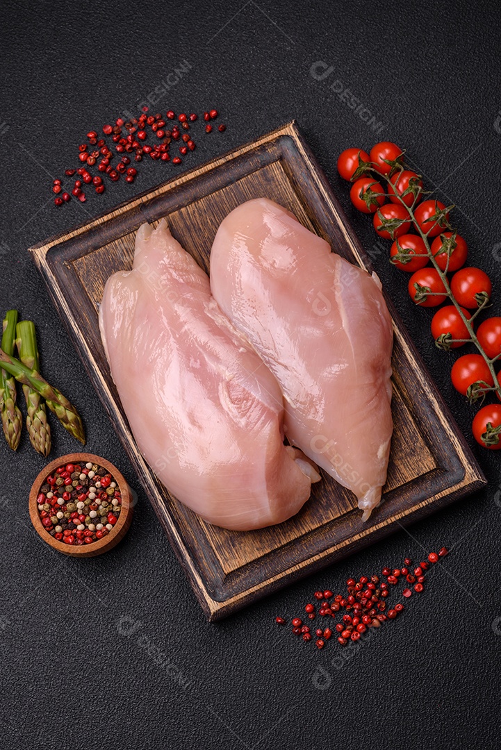 Filé de frango cru com sal, especiarias e ervas sobre um fundo escuro de concreto