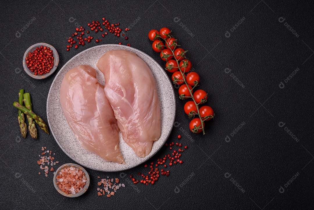 Filé de frango cru com sal, especiarias e ervas sobre um fundo escuro de concreto