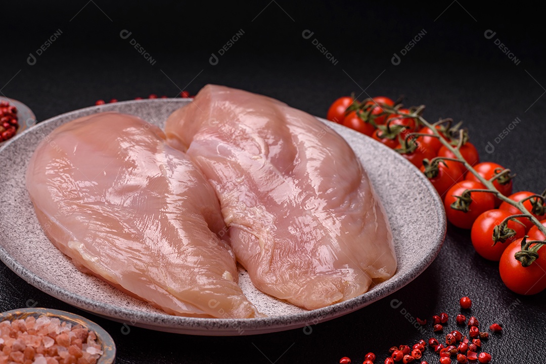 Filé de frango cru com sal, especiarias e ervas sobre um fundo escuro de concreto