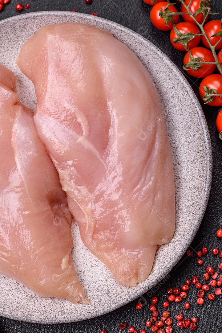 Filé de frango cru com sal, especiarias e ervas sobre um fundo escuro de concreto