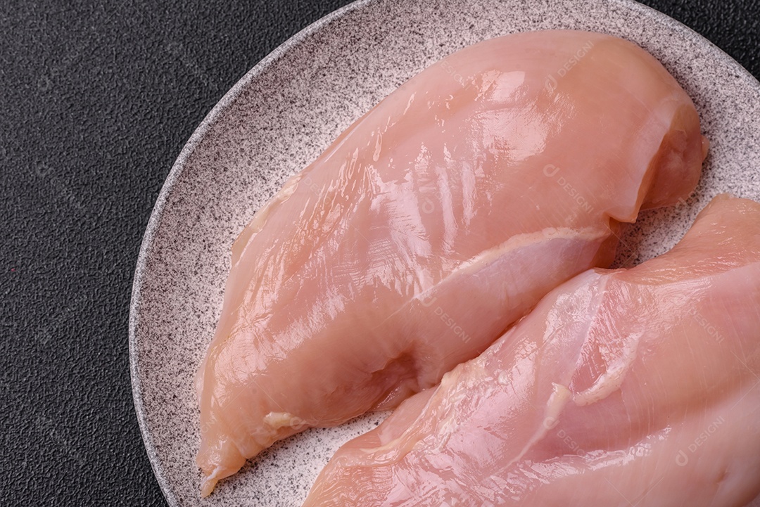 Filé de frango cru com sal, especiarias e ervas sobre um fundo escuro de concreto