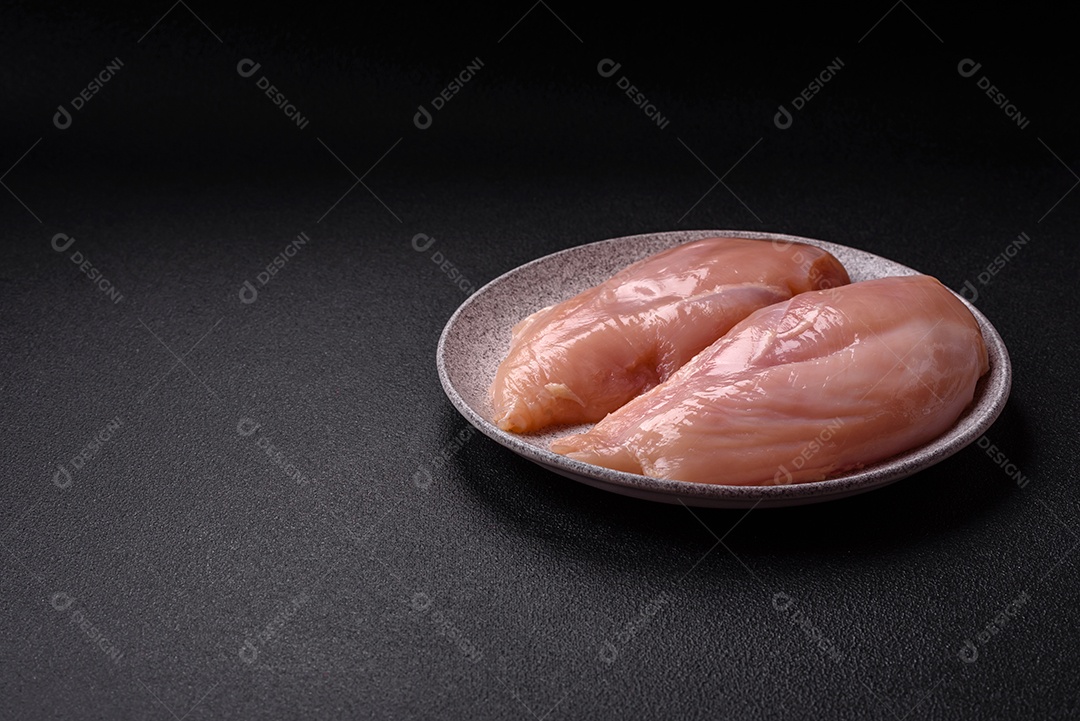 Filé de frango cru com sal, especiarias e ervas sobre um fundo escuro de concreto