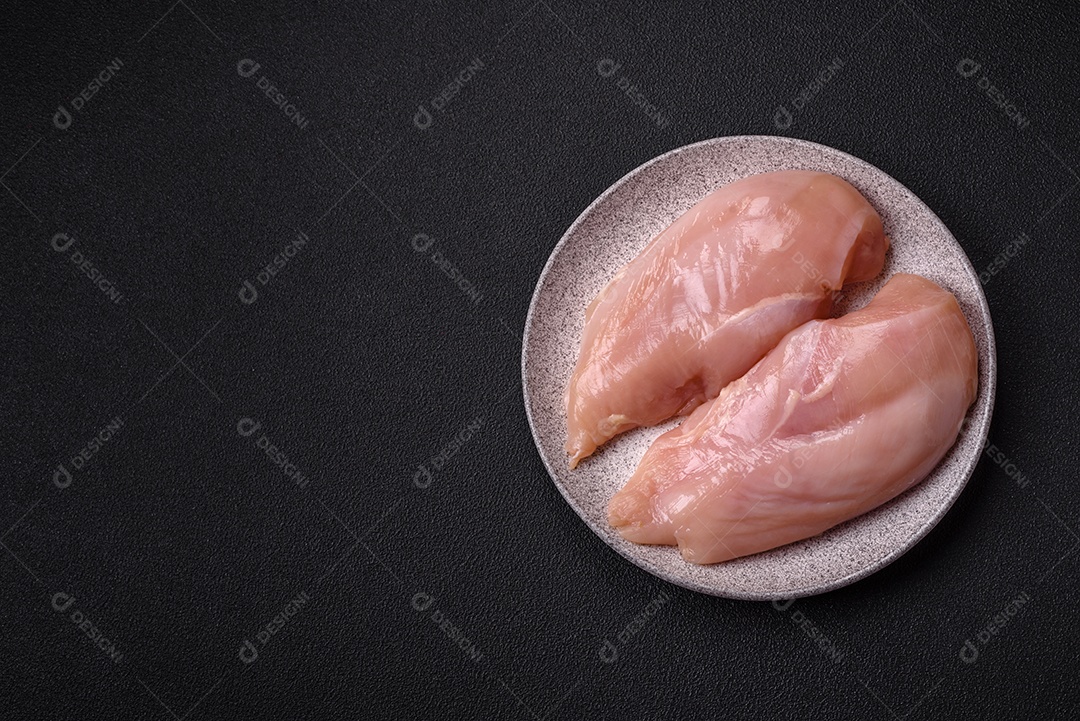 Filé de frango cru com sal, especiarias e ervas sobre um fundo escuro de concreto