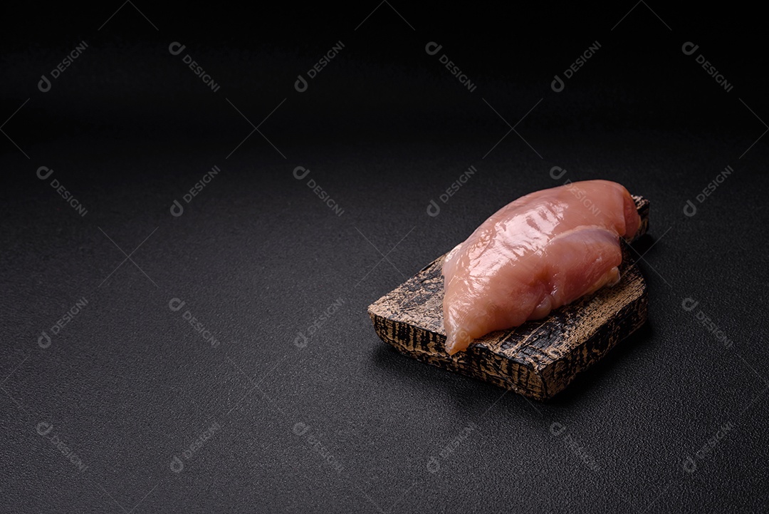 Filé de frango cru com sal, especiarias e ervas sobre um fundo escuro de concreto