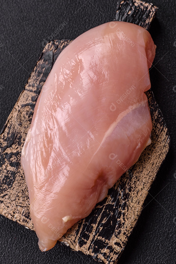 Filé de frango cru com sal, especiarias e ervas sobre um fundo escuro de concreto