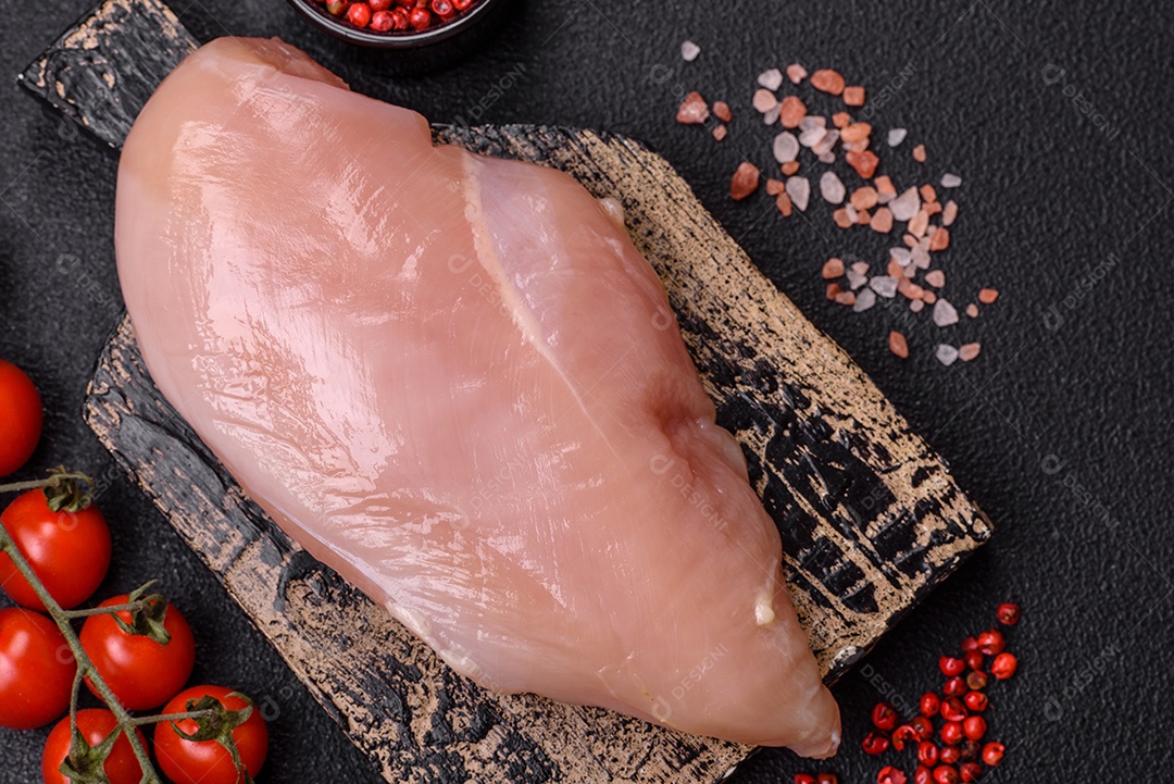 Filé de frango cru com sal, especiarias e ervas sobre um fundo escuro de concreto