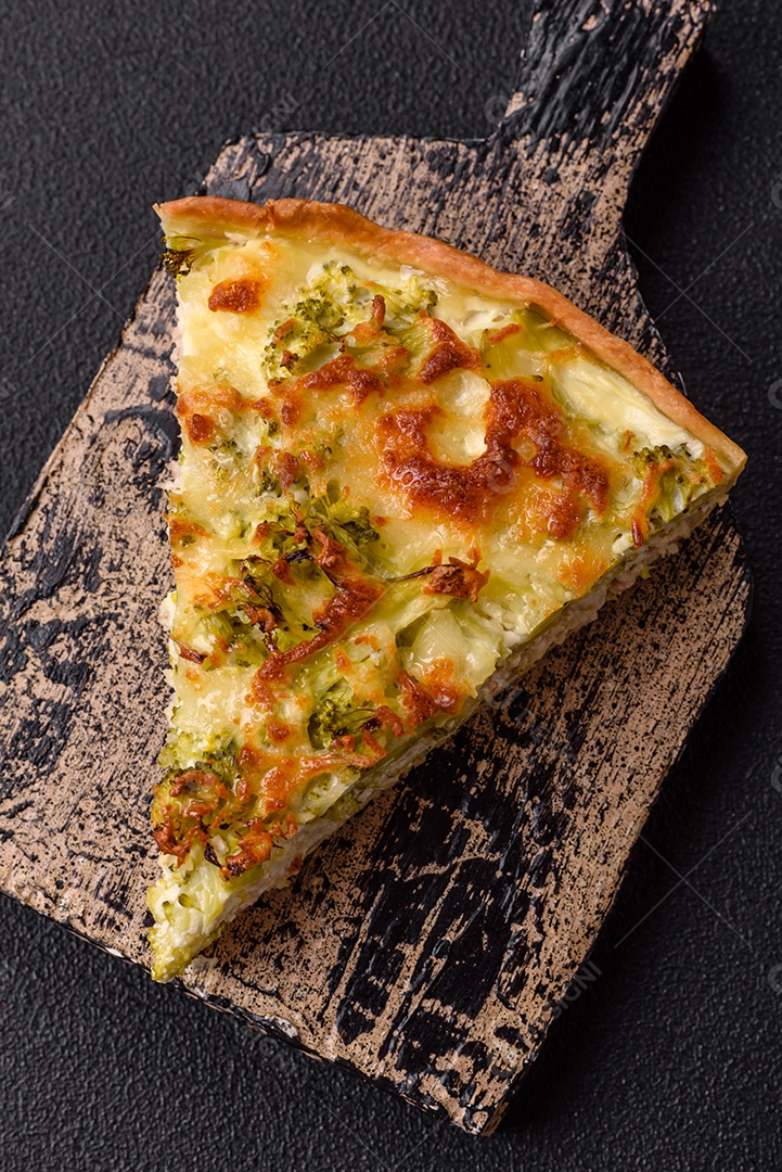 Deliciosa quiche com brócolis, queijo, frango, especiarias e ervas sobre um fundo escuro de concreto