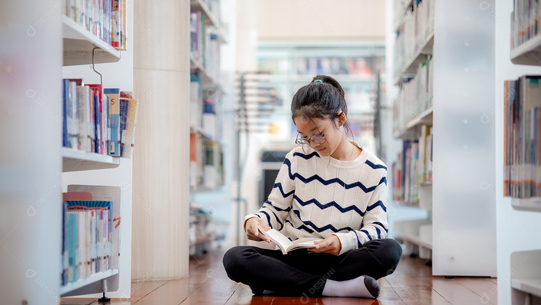 Uma garota sentada no chão dedicada a ler um livro