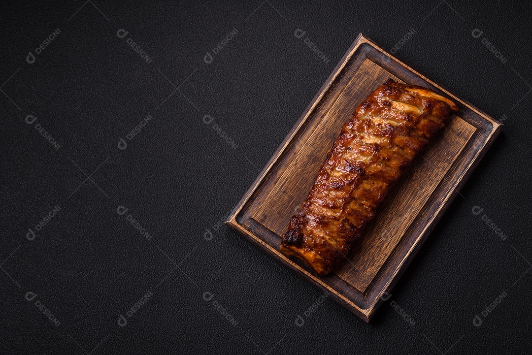 Deliciosas costelas grelhadas suculentas com mel e molho de mostarda com sal, especiarias e ervas sobre um fundo escuro de concreto