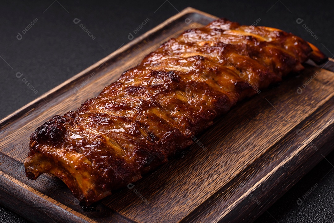 Deliciosas costelas grelhadas suculentas com mel e molho de mostarda com sal, especiarias e ervas sobre um fundo escuro de concreto