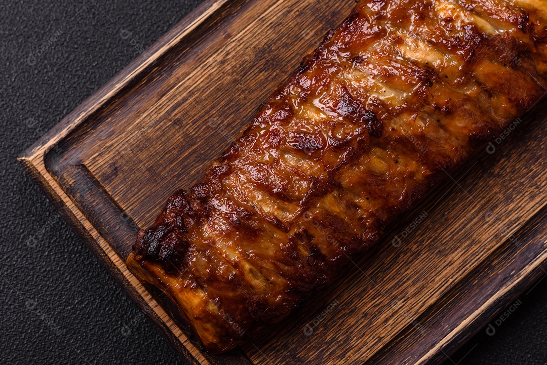 Deliciosas costelas grelhadas suculentas com mel e molho de mostarda com sal, especiarias e ervas sobre um fundo escuro de concreto